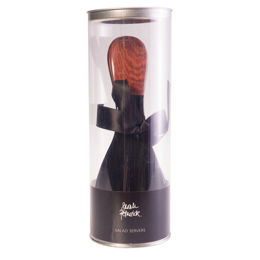 A pair of black water buffalo horn salad servers with rosewood handles, packaged in a clear tube