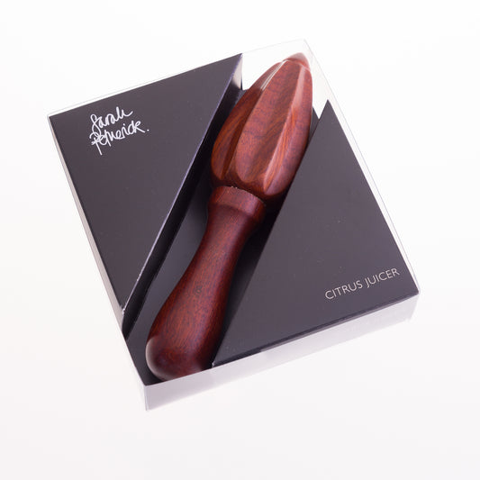 A rosewood citrus reamer packaged in a square clear box with a black insert