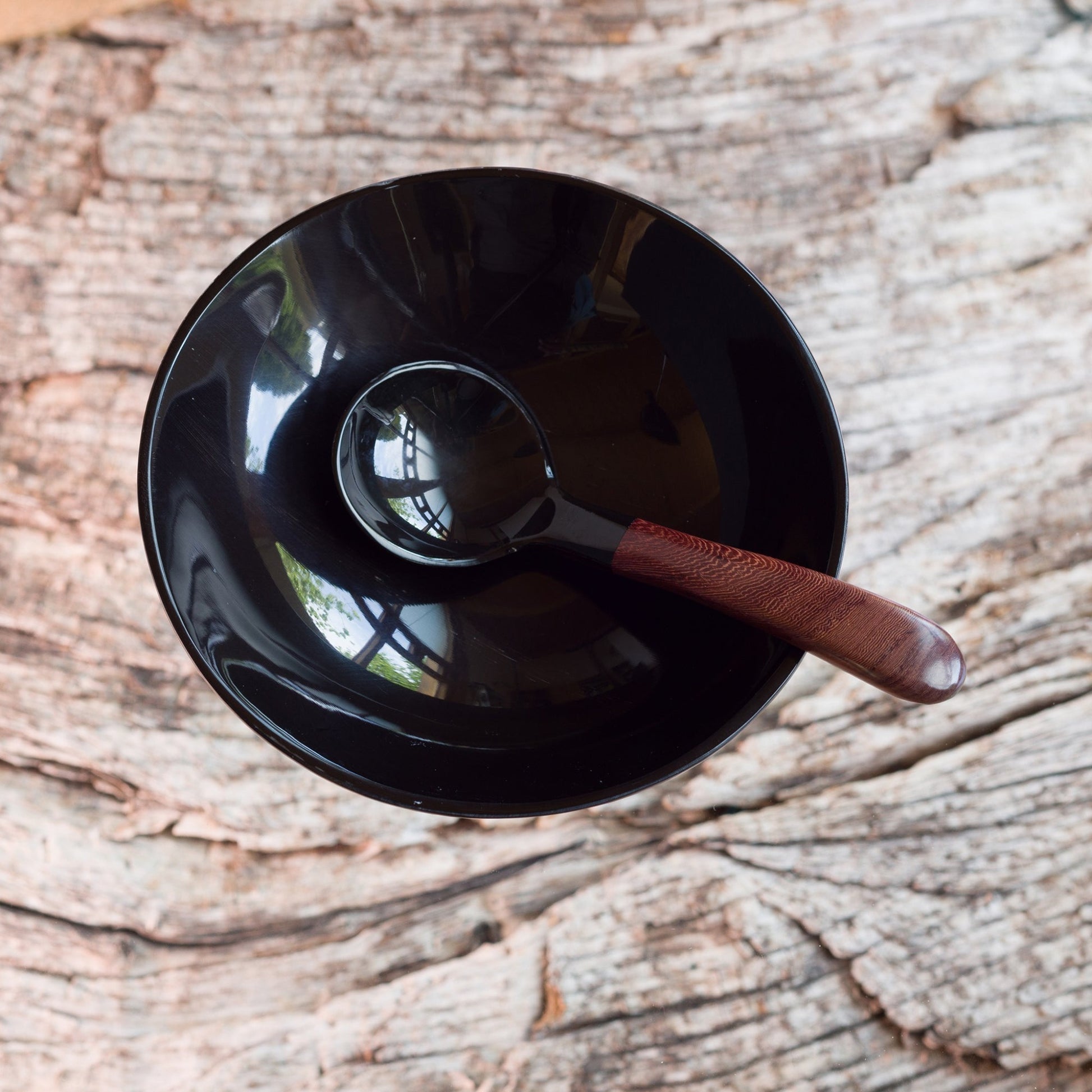 A small ladle made from water buffalo horn with a rosewood handle sitting in a round horn bowl