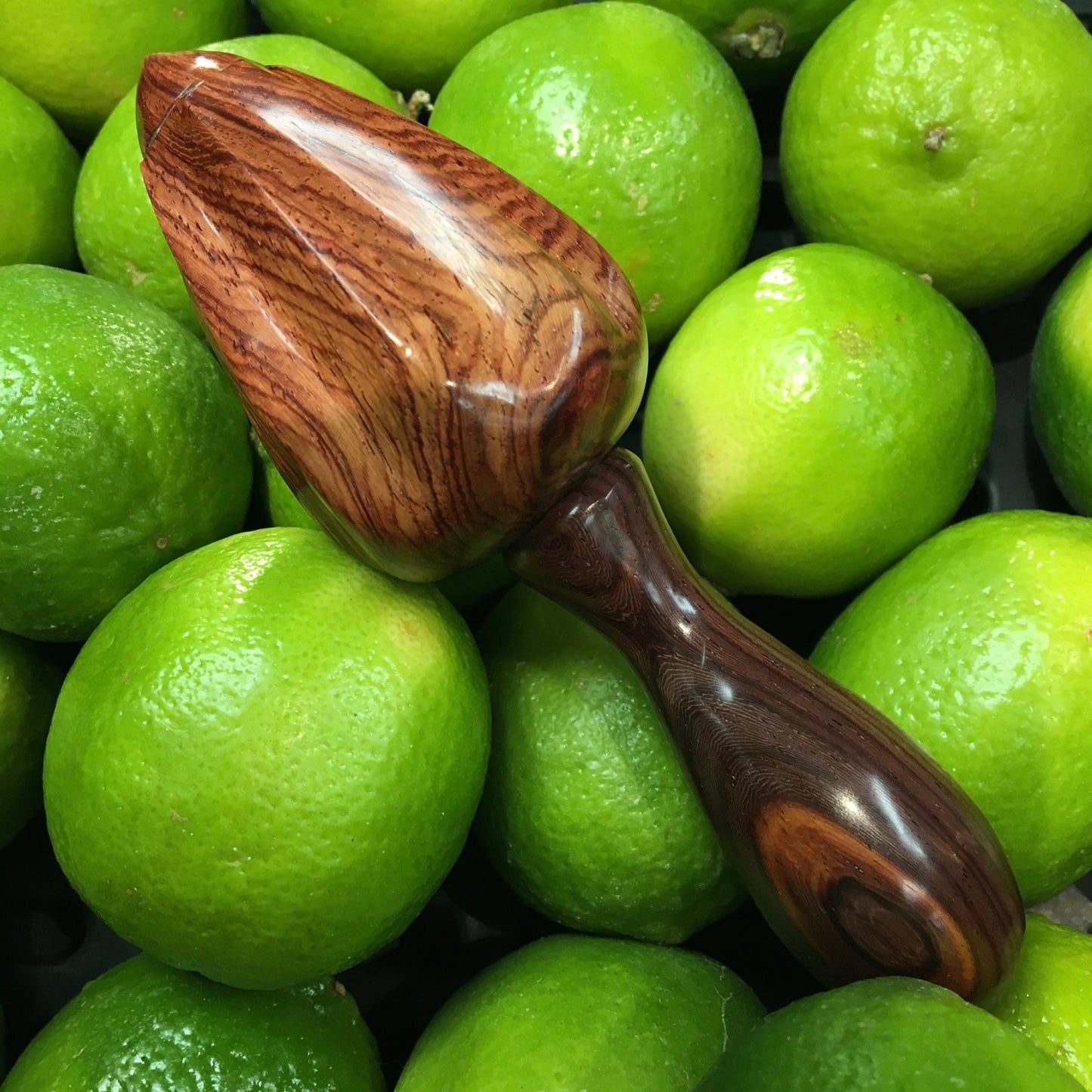 A rosewood citrus reamer sitting on a pile of limes